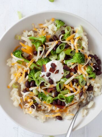 A loaded potato bowl topped with shredded cheese, black beans, scallions and more.