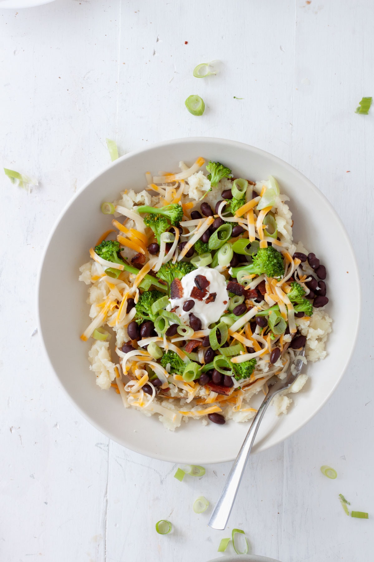 A loaded potato bowl topped with shredded cheese, black beans, scallions and more.