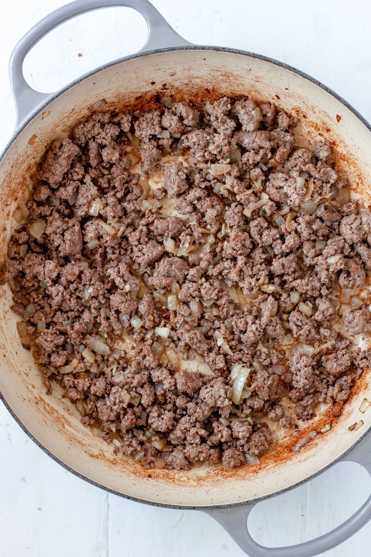 Ground beef and onions cooking in a large skillet.
