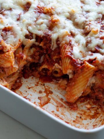 A baking dish with rigatoni al forno and a piece taken out of the pasta dish.
