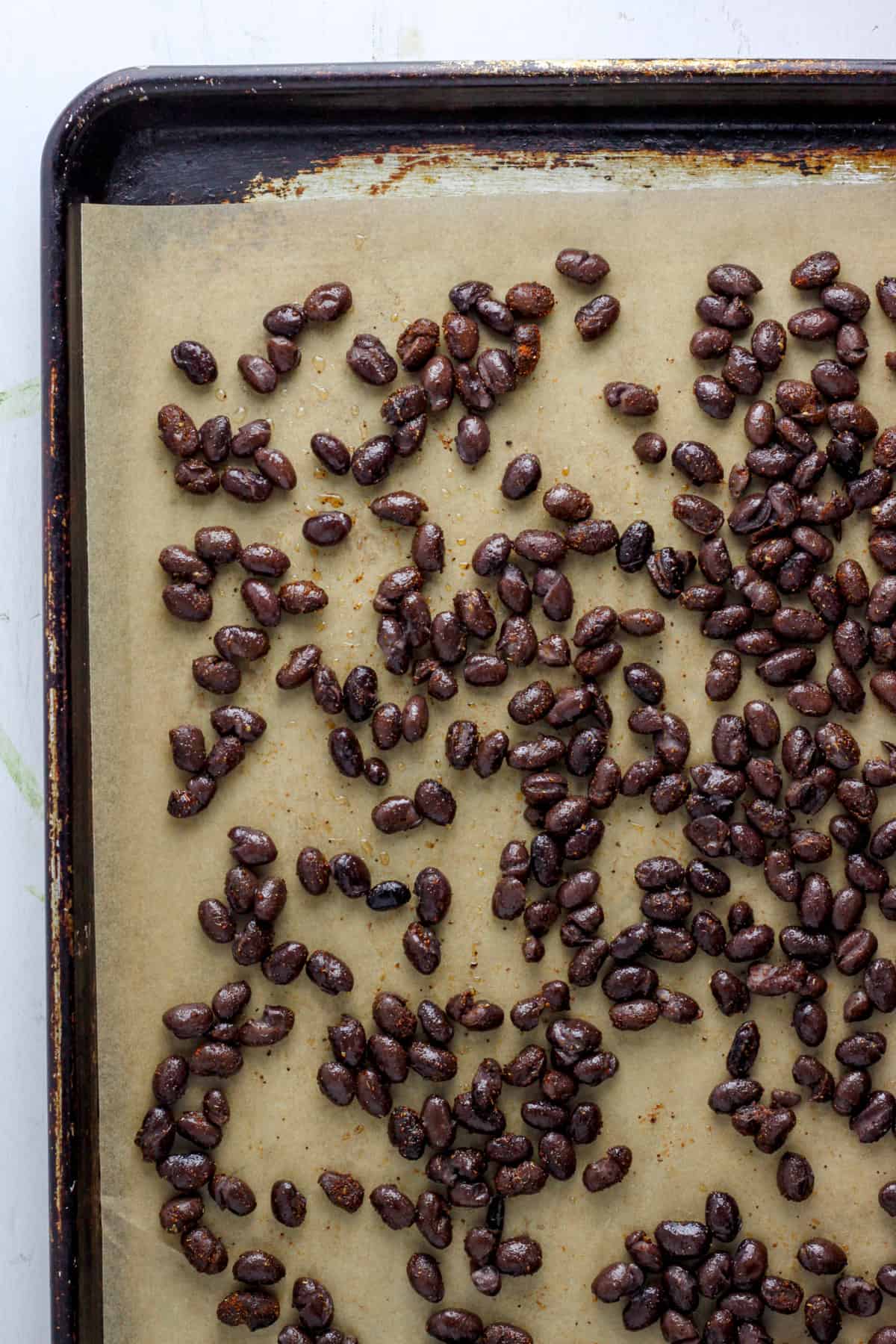 A baking sheet with parchment and black beans on top ready to be roasted.