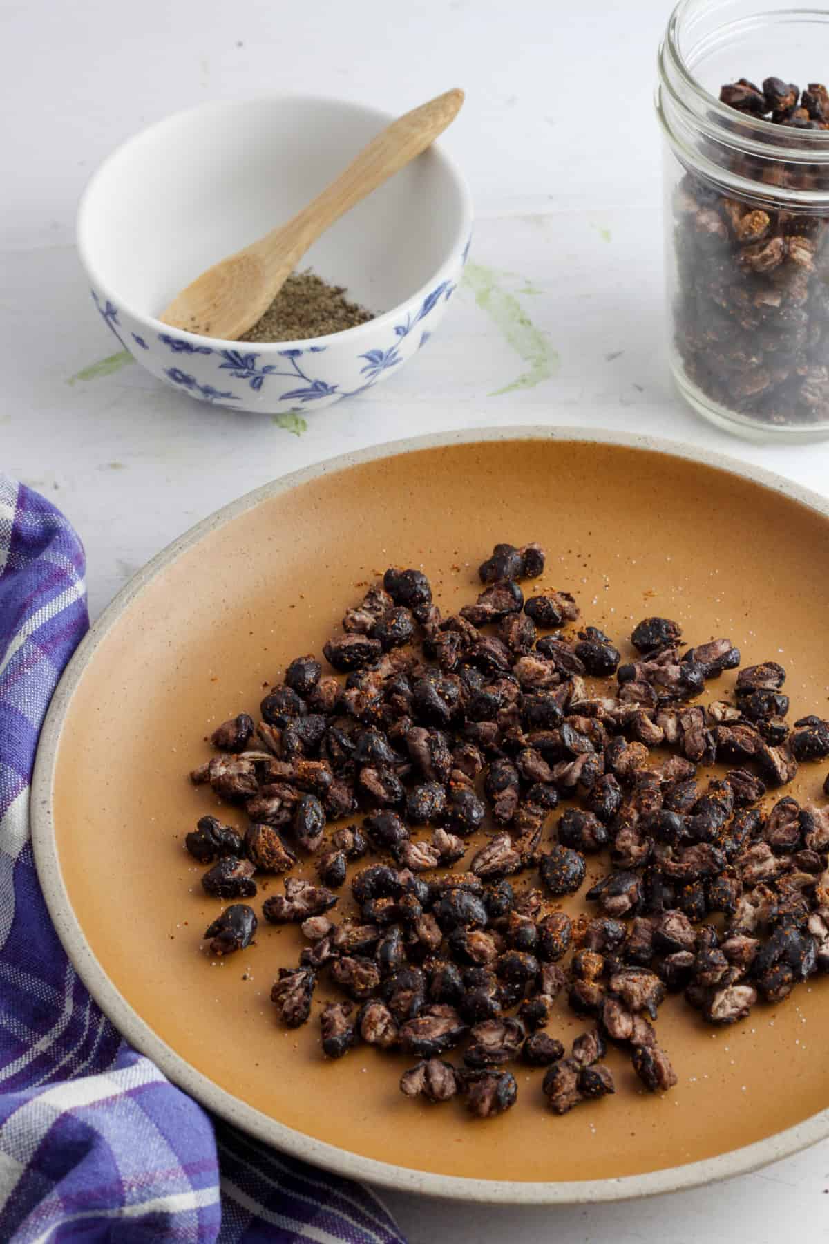 A plate of roasted black beans with more beans in the background in a mason jar.
