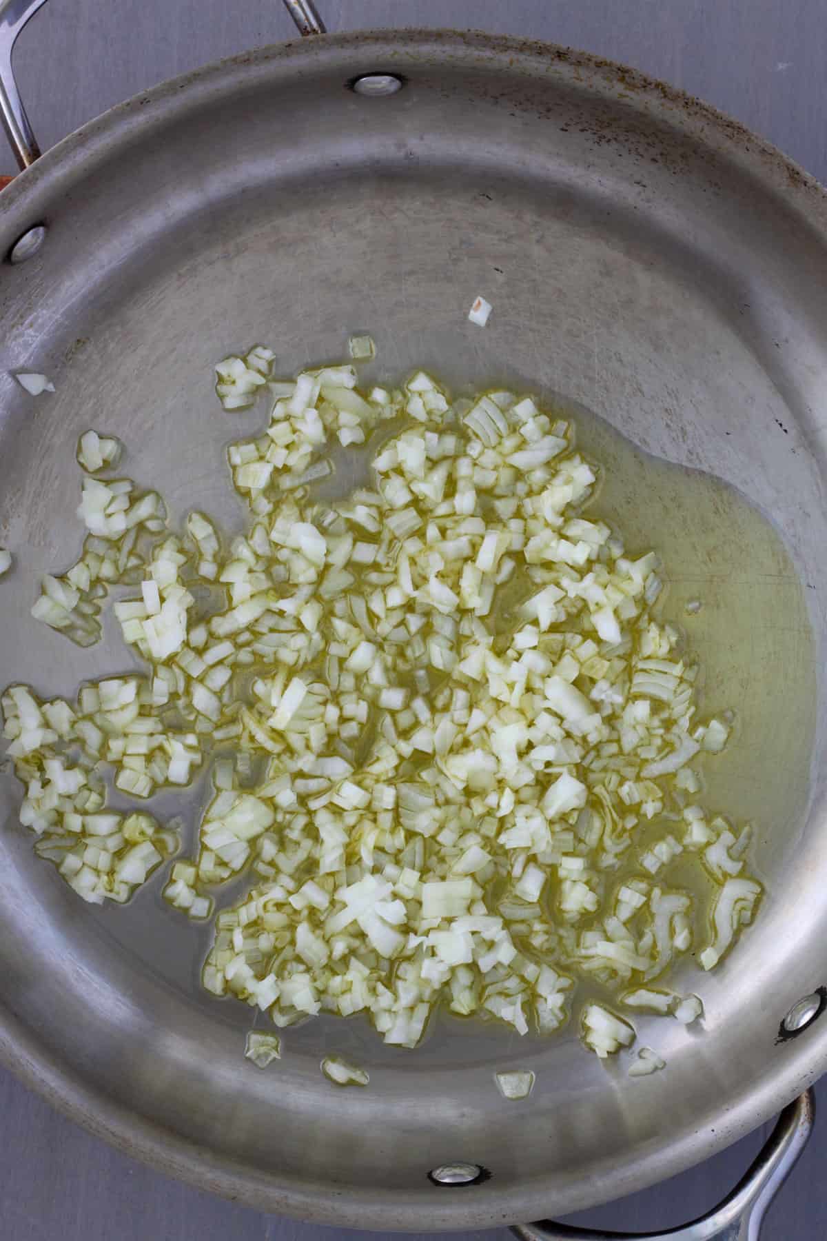 A large skillet with olive oil and finely chopped onion cooking.