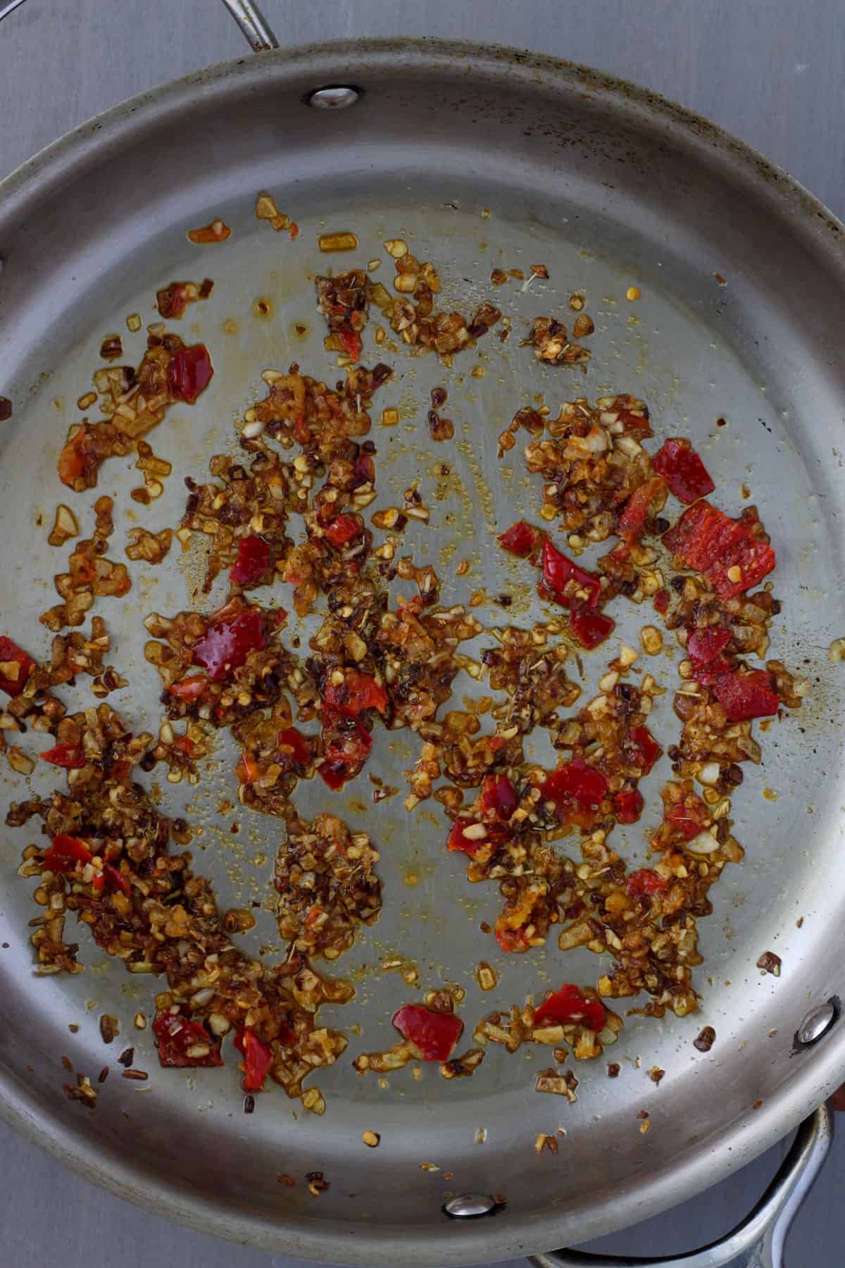 A large skillet with oil, browned onions, garlic, spices and Calabrian chili peppers.