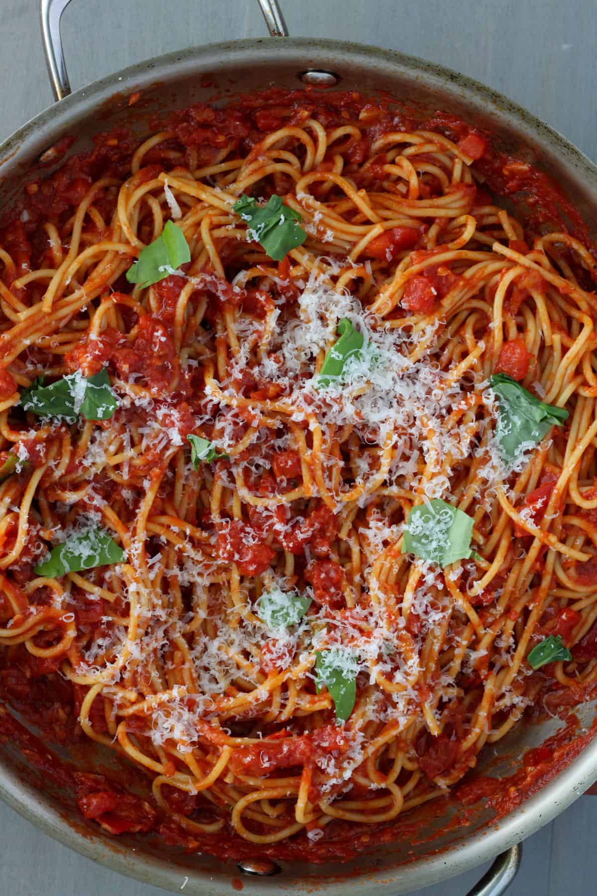 A large skillet with spaghetti arrabiata topped with basil and grated parmesan.