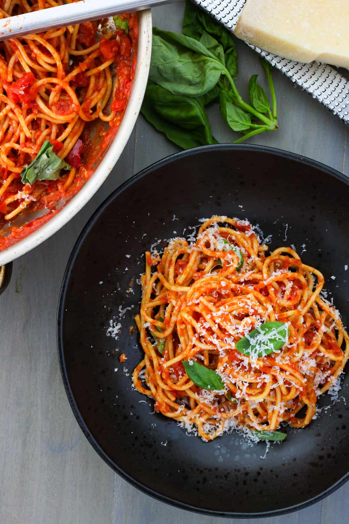 A black bowl with spaghetti arrabiata topped with basil and grated parmesan.