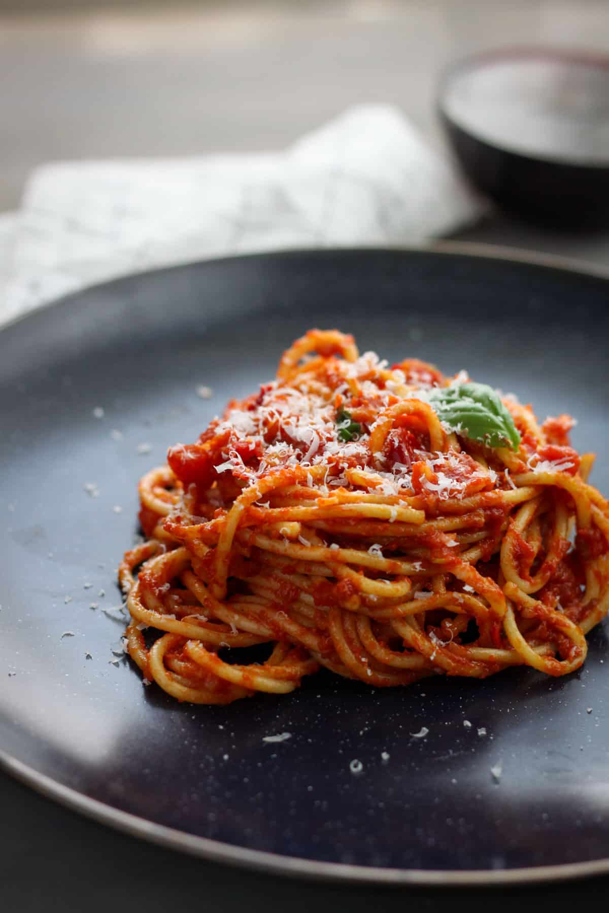 A plate of spaghetti arrabiata topped with basil and grated parmesan.