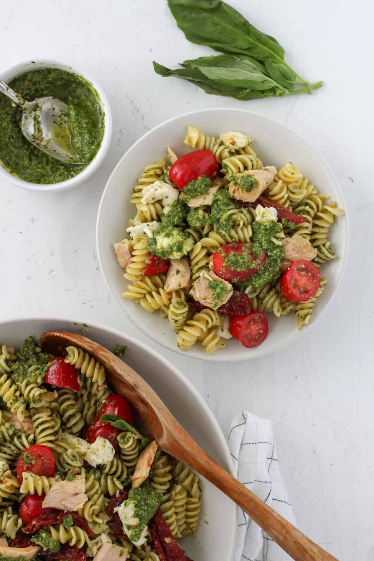 A small bowl of tuna pesto pasta with a large bowl off center and a small bowl of pesto off center.