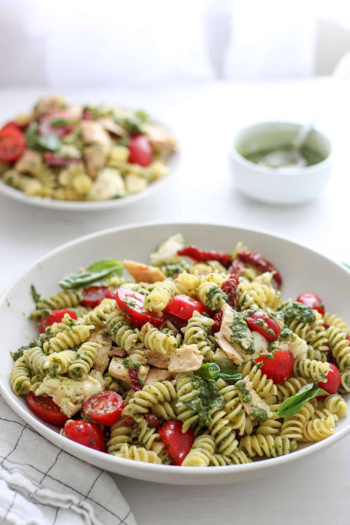 A large bowl of tuna pesto pasta with another small bowl in the background with another bowl of pesto in the background.