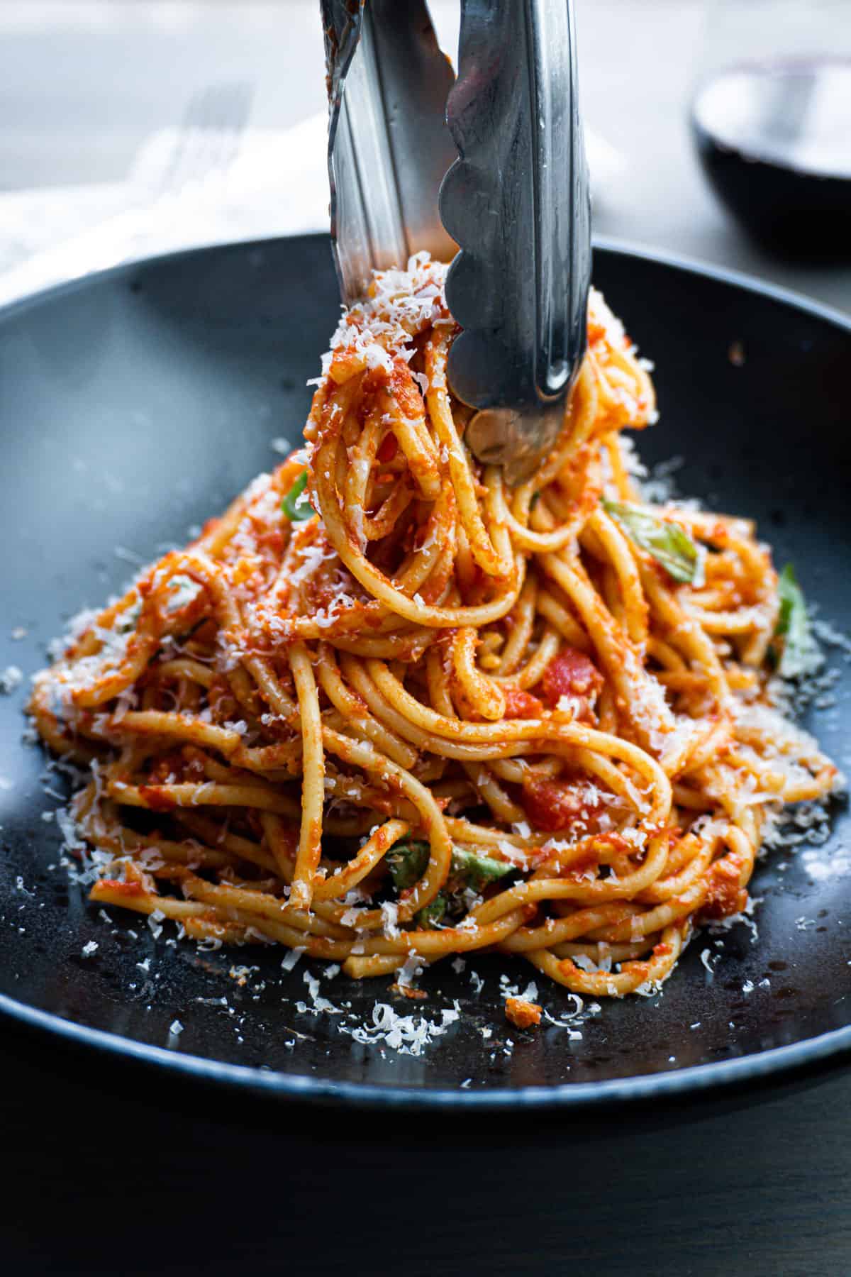 A plate of spaghetti arrabiata getting served with tongs.
