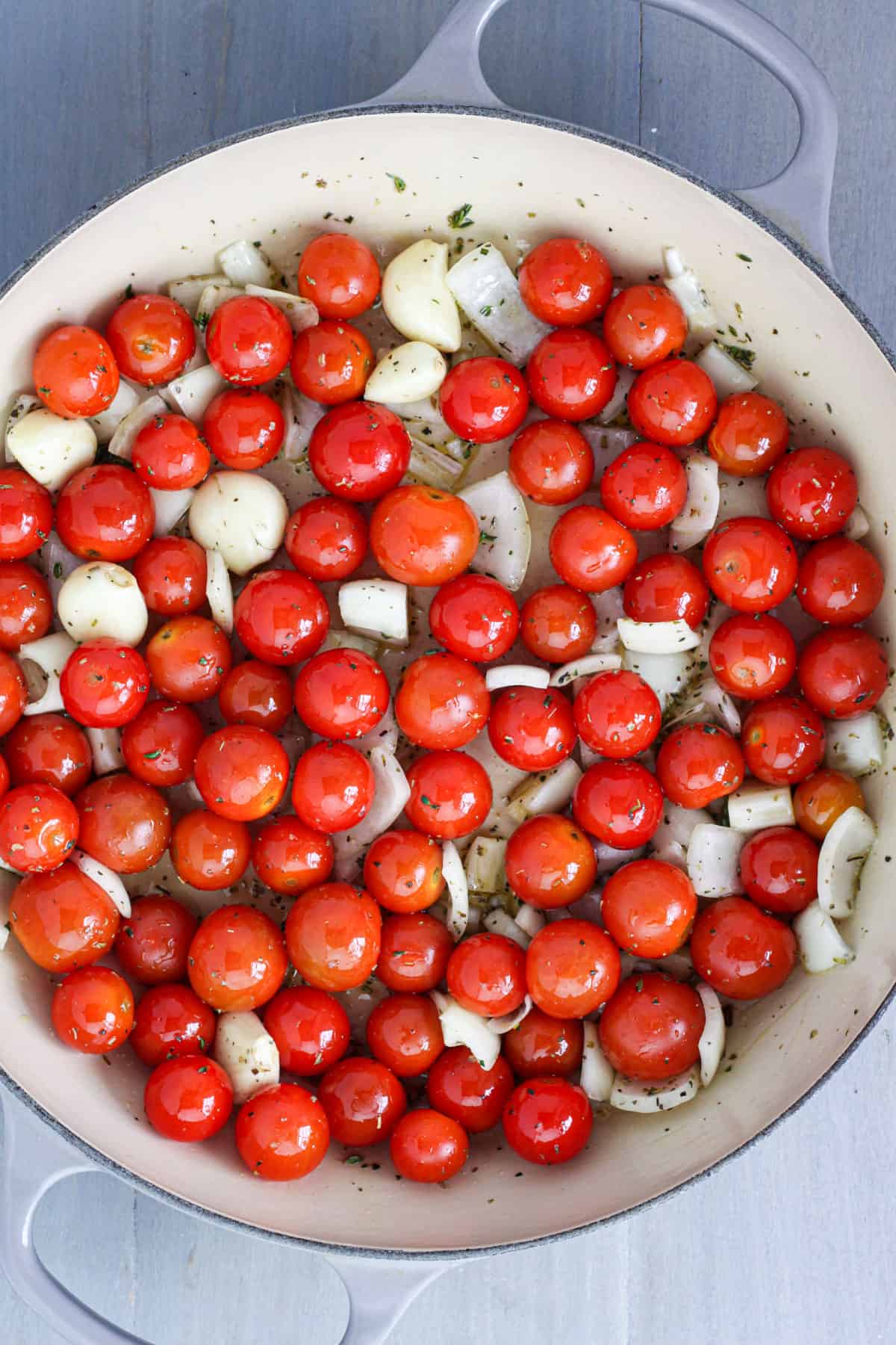 Cherry tomatoes, onions, garlic, herbs and oil in a skillet.