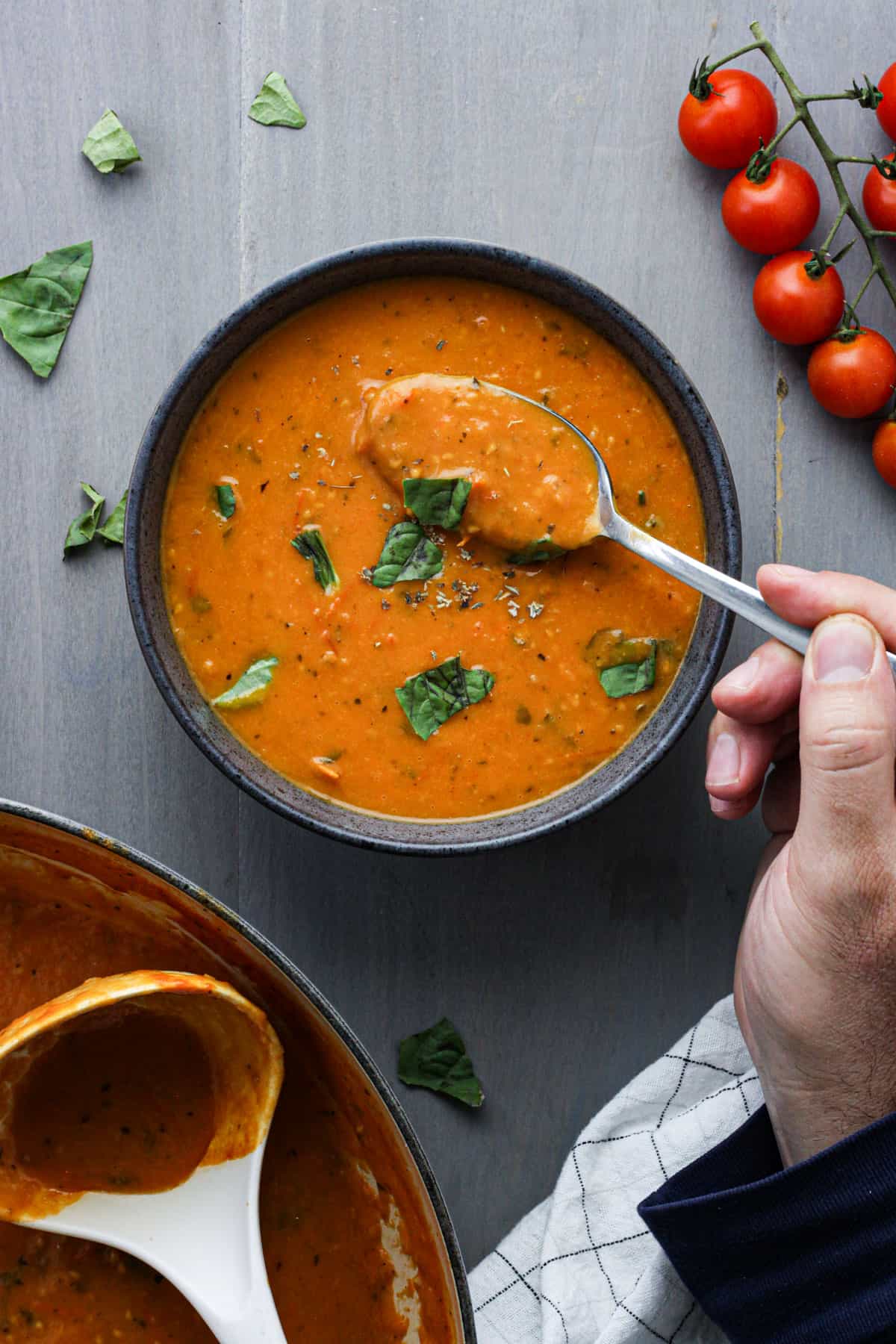 Cherry Tomato Soup in a gray bowl with a hand taking a spoonful of the soup.