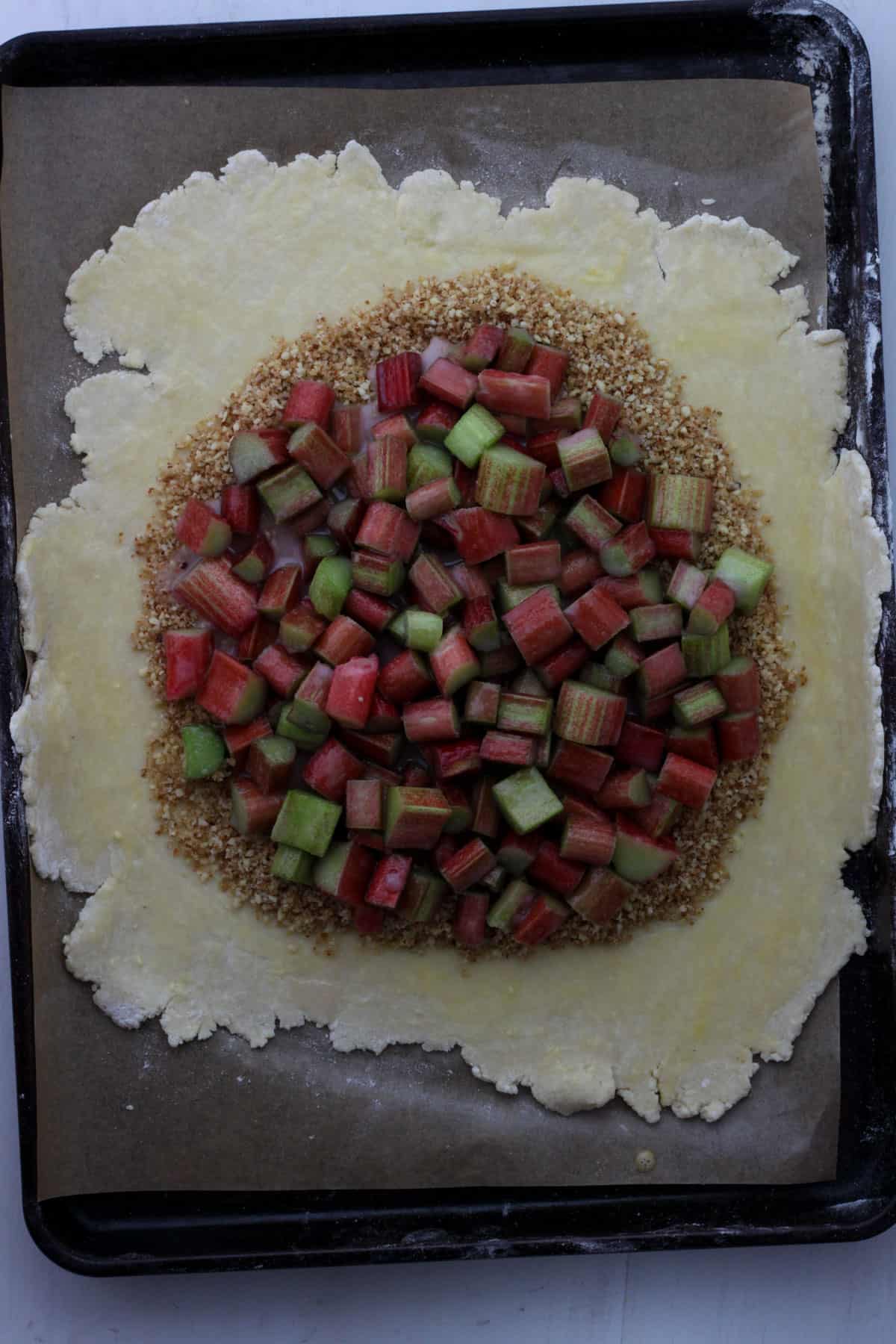 Pie crust with almonds on top in the center and chopped rhubarb and sugar on top of the almonds.