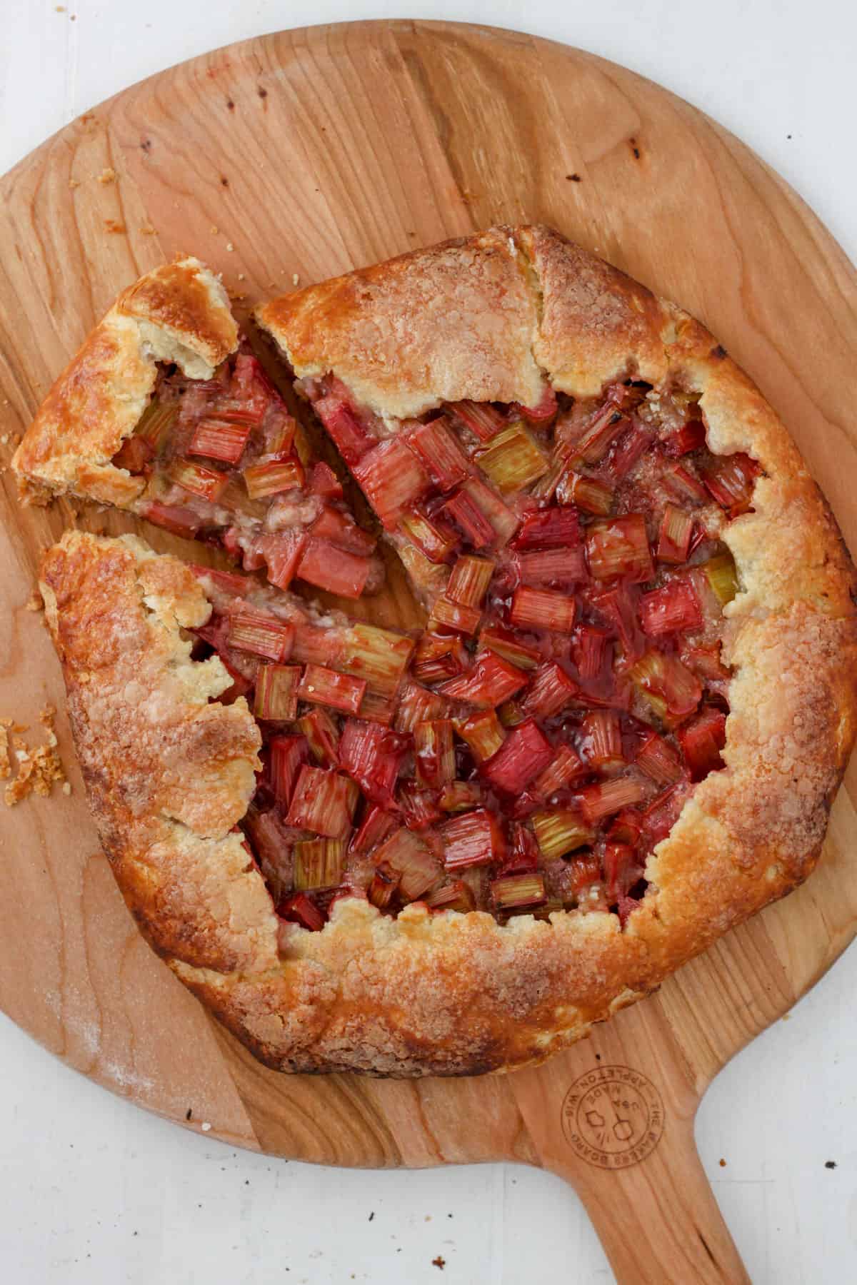 Rhubarb galette with a piece cut out on a wooden pizza peel.