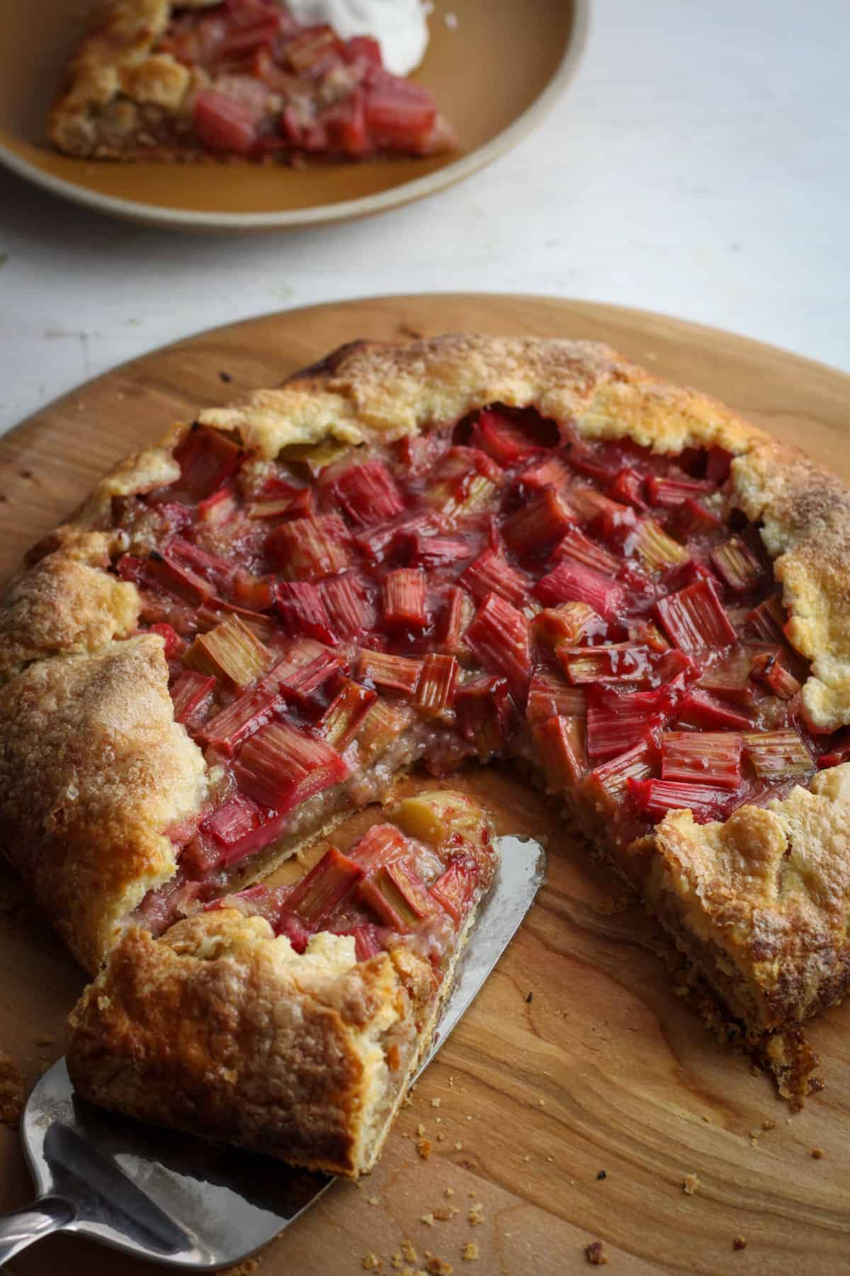A rhubarb galette on a wooden pizza peel with a slice taken out.