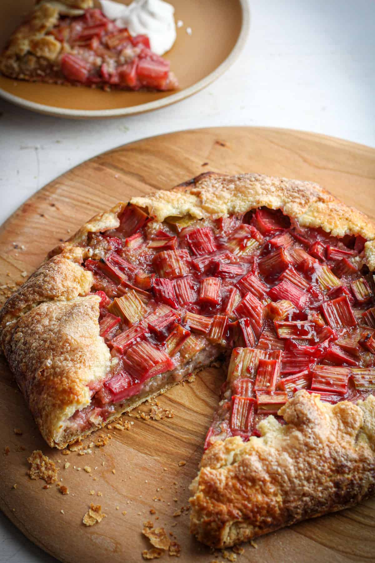 A rhubarb galette on a wooden pizza peel with a slice taken out.