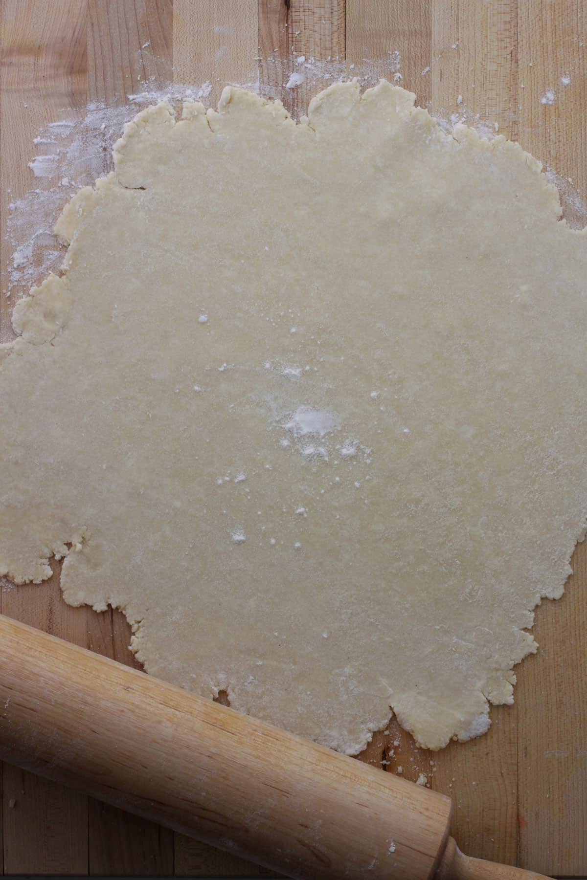 Pie crust rolled out on a cutting board with a rolling pin nearby.