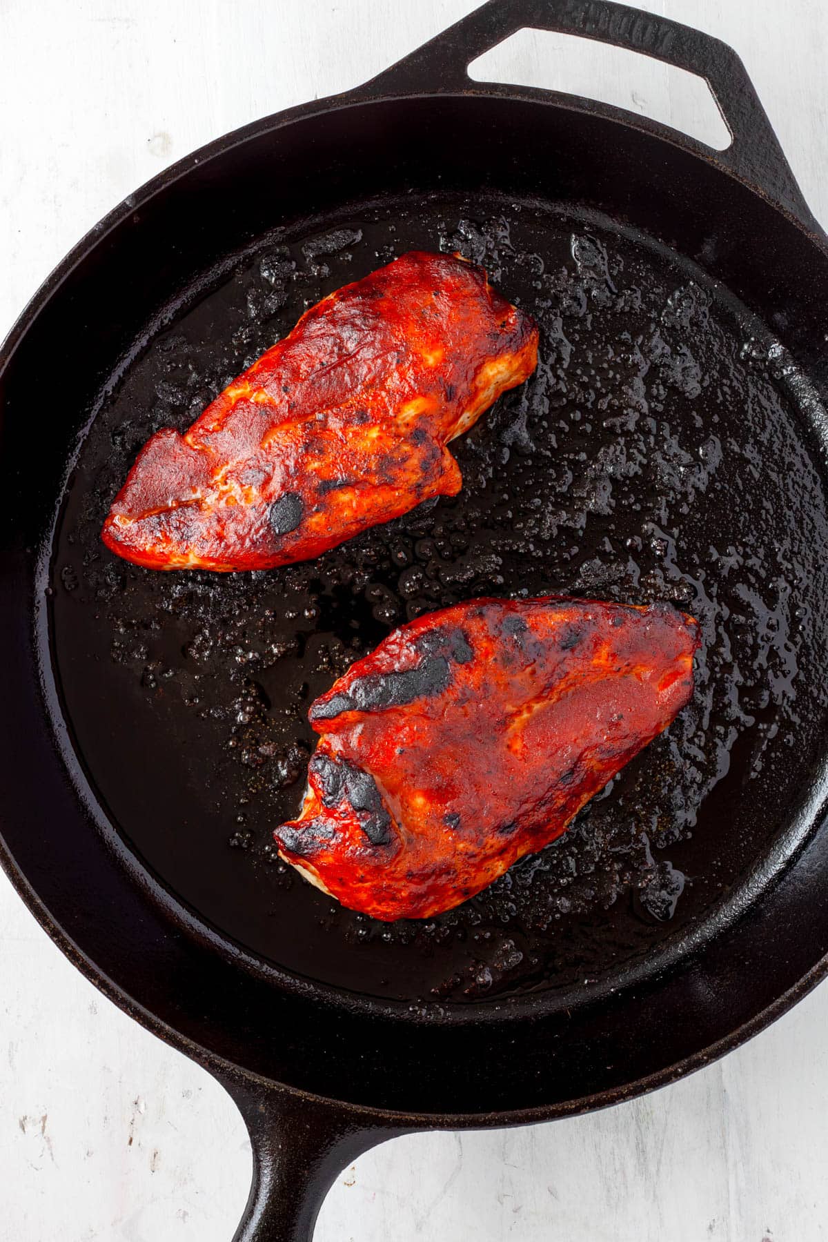 BBQ cast iron skillet chicken charred and brushed with more sauce.