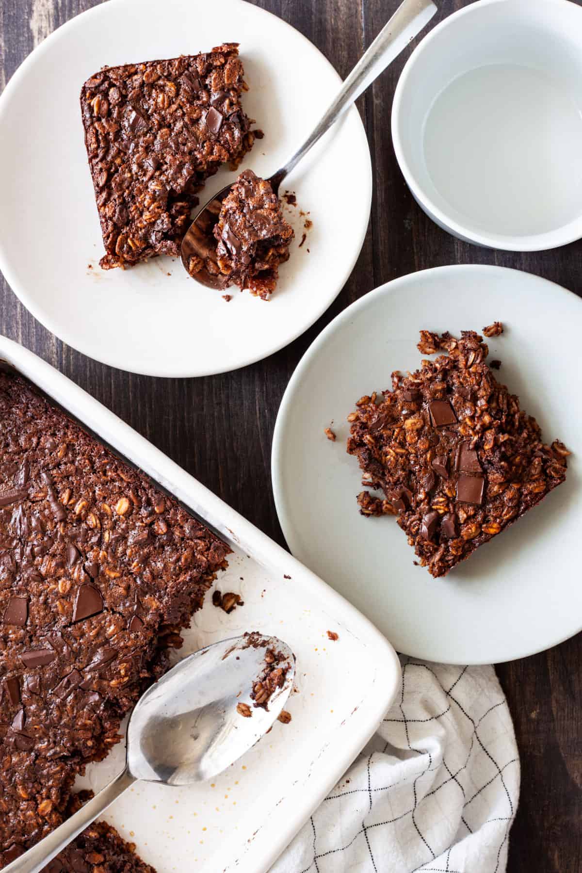 A baking dish of chocolate baked oatmeal with two portions on small plates.