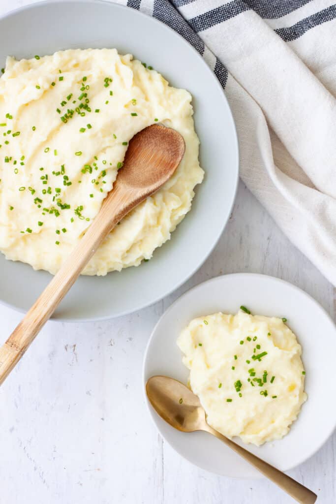 Yukon gold mashed potatoes with sour cream in a large bowl with a serving in a smaller bowl.