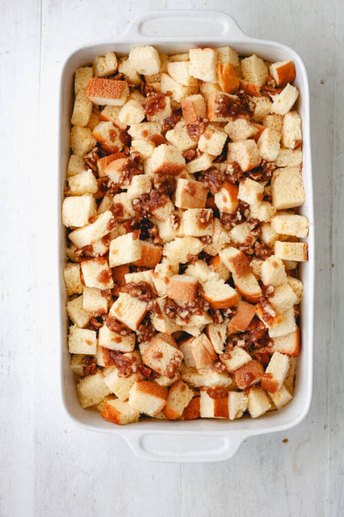A brioche French toast casserole getting assembled with a brown sugar and pecan topping.