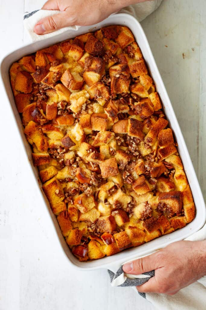 Hands with towels carrying a hot out of the oven brioche French toast casserole.