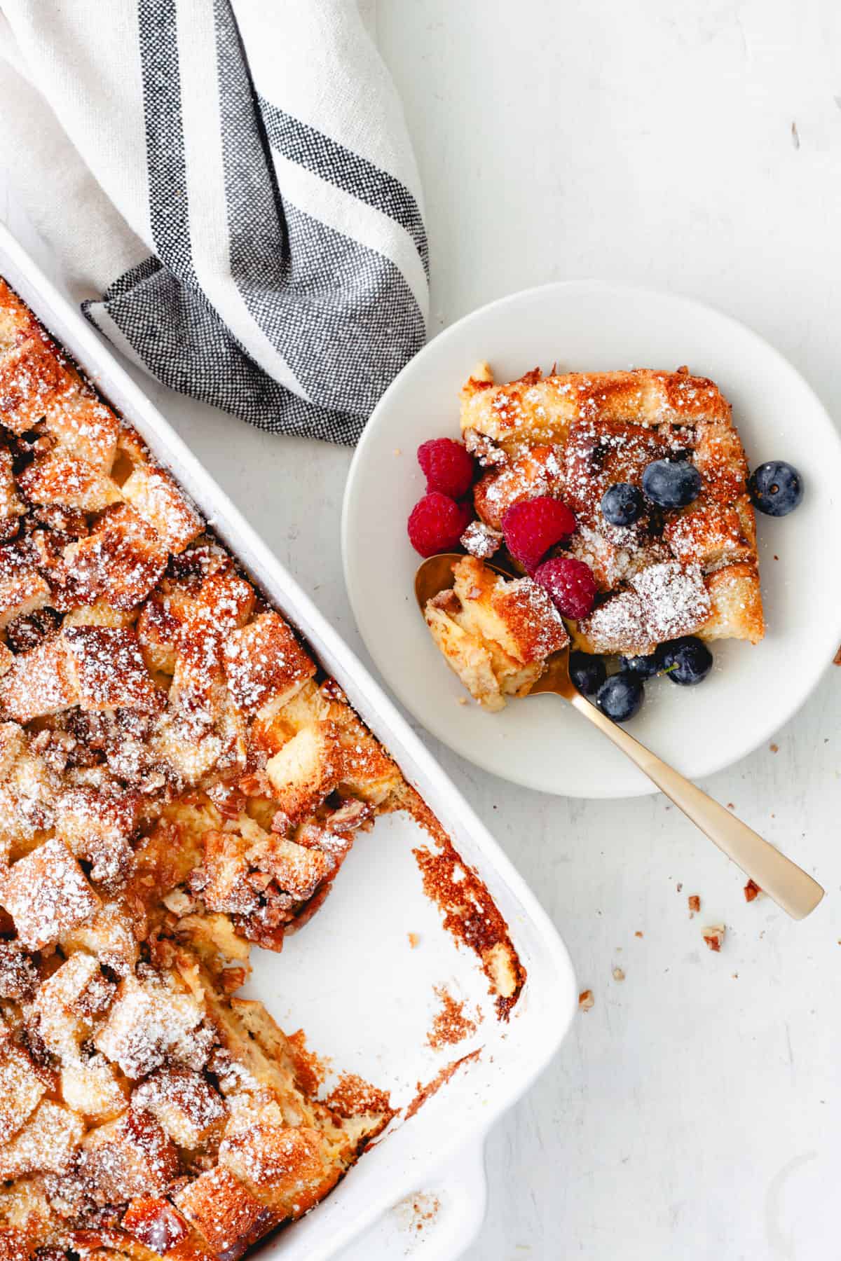 A piece of brioche French toast casserole on a small plate with the casserole dish in the background.