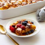 A piece of brioche French toast casserole on a small plate with the casserole dish in the background.
