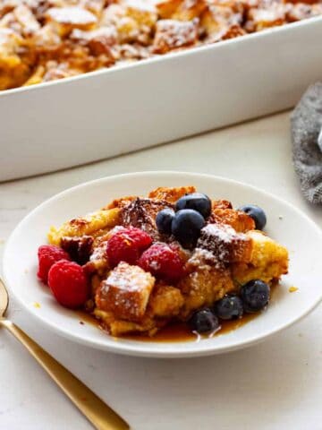A piece of brioche French toast casserole on a small plate with the casserole dish in the background.