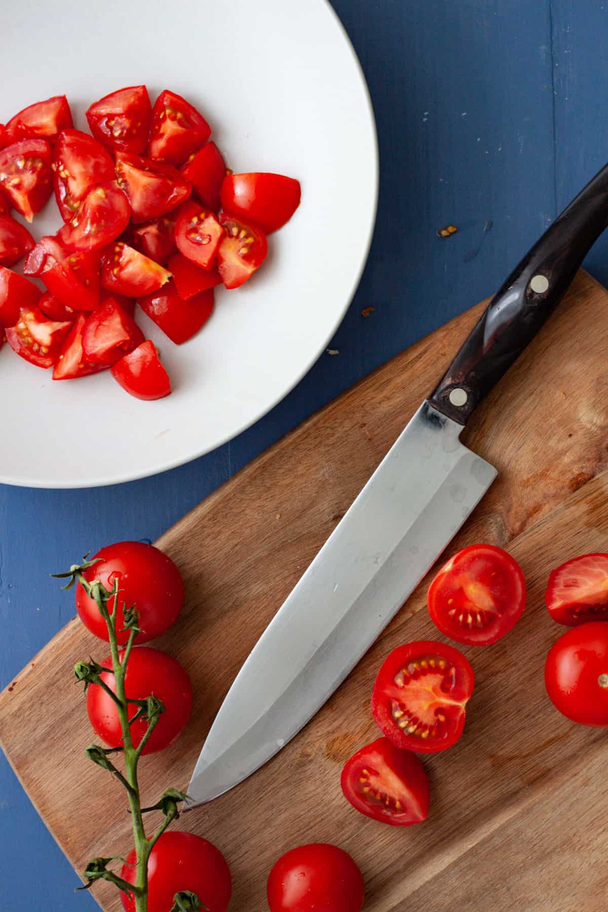 Cherry tomatoes getting sliced on a cutting board.