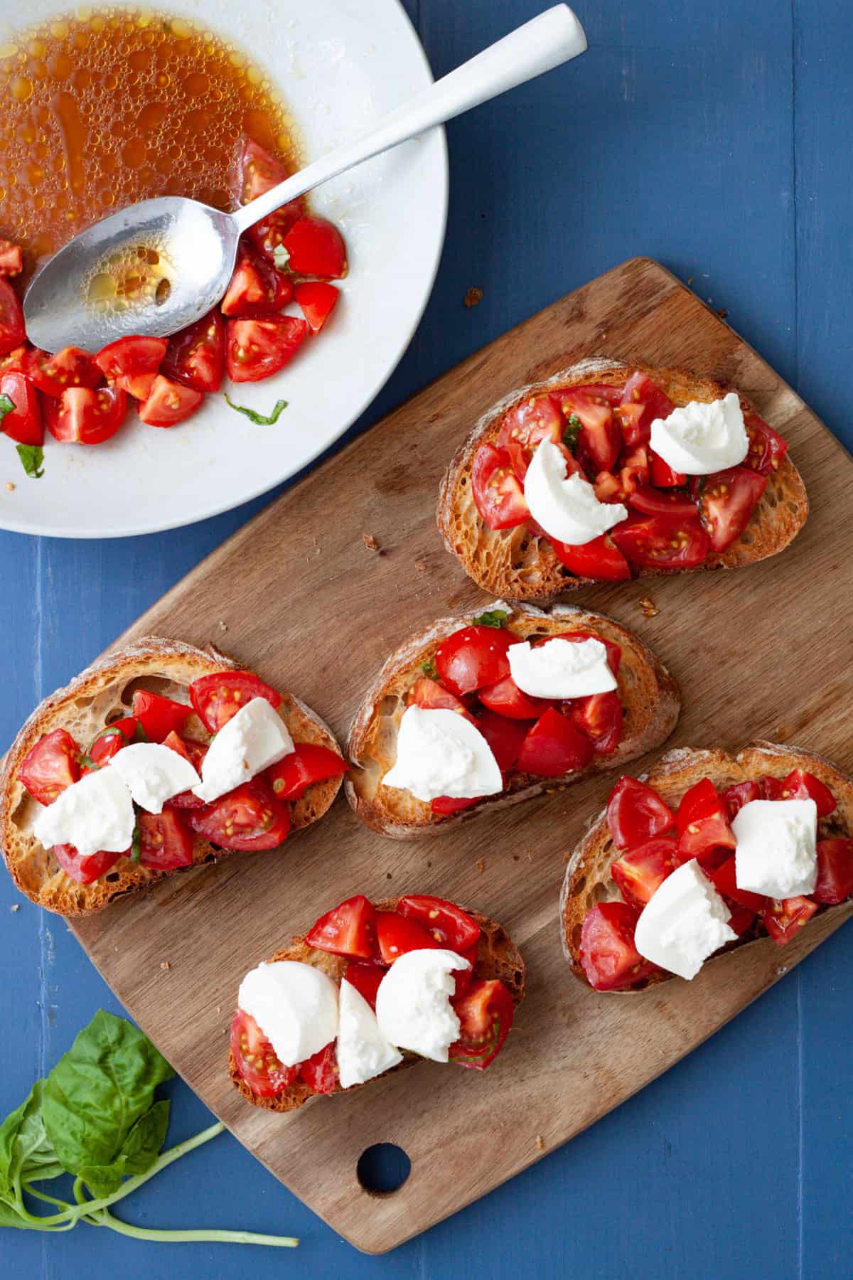 Burrata bruschetta getting assembled on a cutting board.