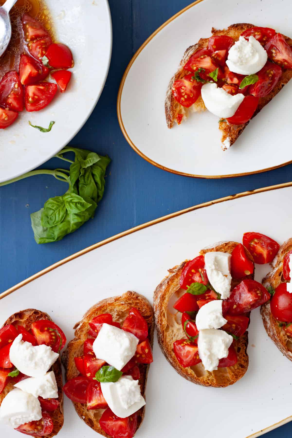 A platter of burrata bruschetta on a white plate with a single portion on a smaller plate.