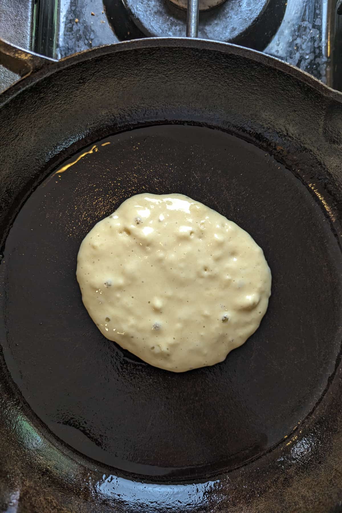 Oat milk pancakes just added to a cast iron skillet.