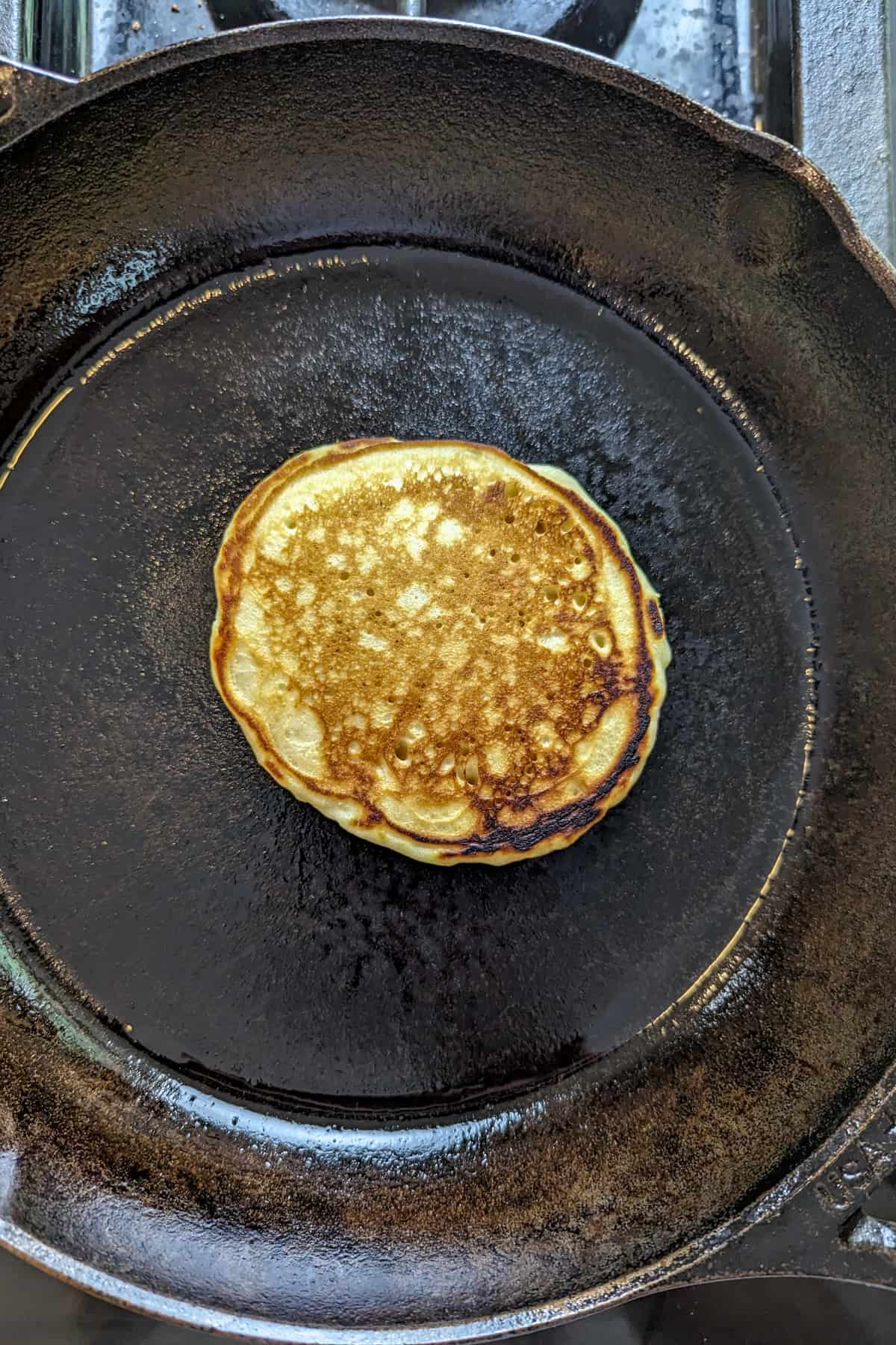An oat milk pancake cooking in a cast iron skillet.