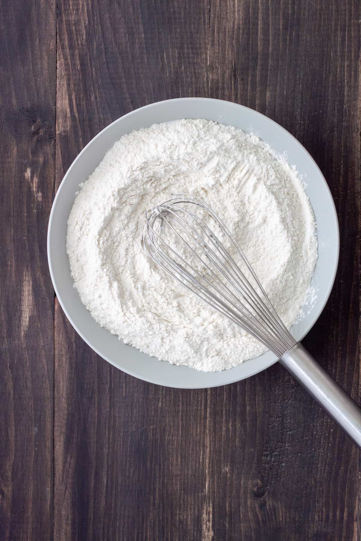 Dry ingredients for oat milk pancakes in a mixing bowl with a whisk.