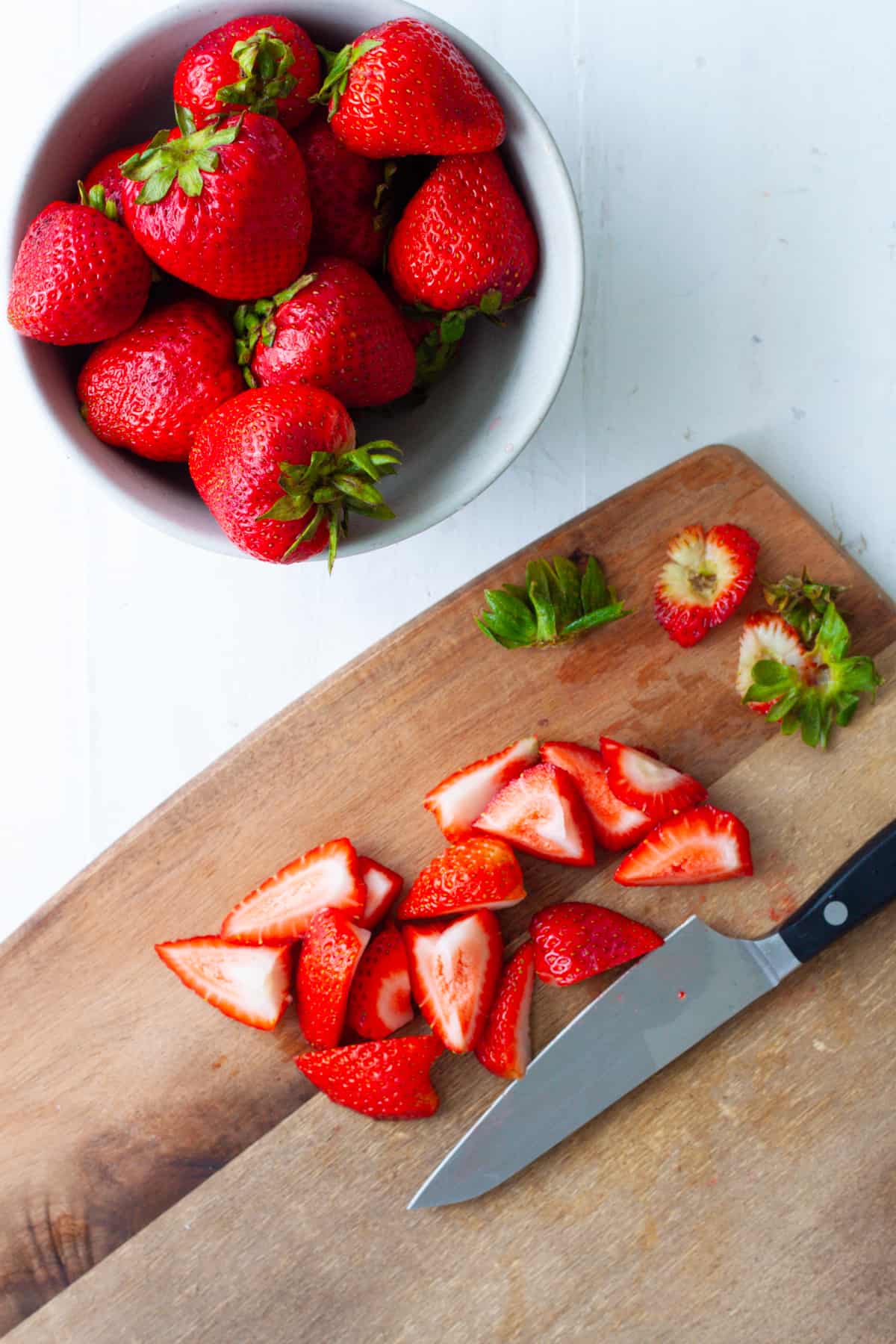 Strawberries getting cut on a wooden cutting board.