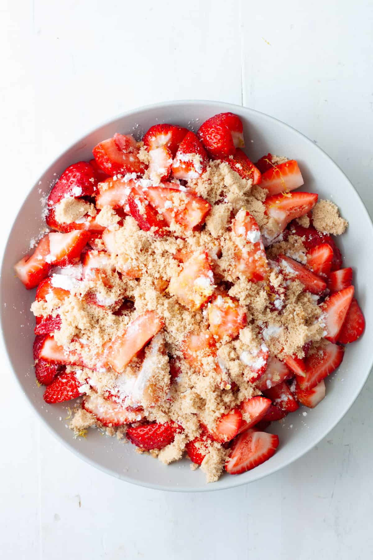 Sliced strawberries in a mixing bowl with sugar and lemon juice on top.