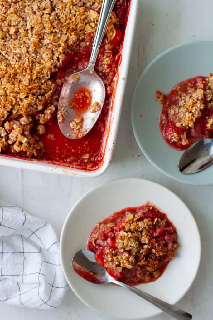 Two plates of strawberry crumble and a baking dish with more crumble off to the side.