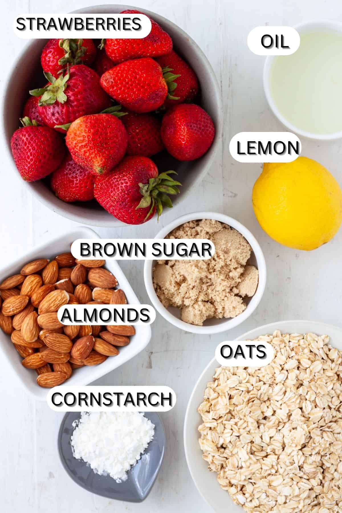 Ingredients for a strawberry crumble on a table and in small bowls.