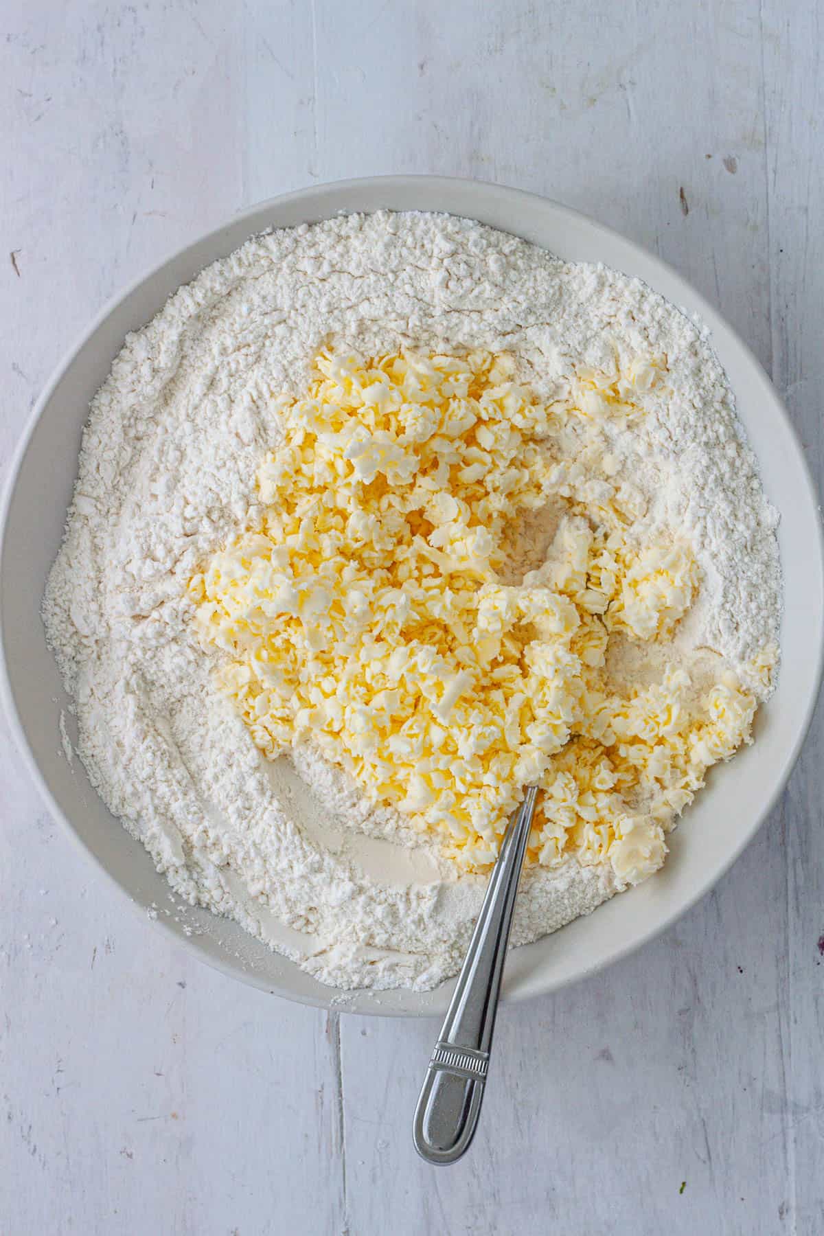 Grated butter in a bowl with the dry ingredients for drop biscuits.