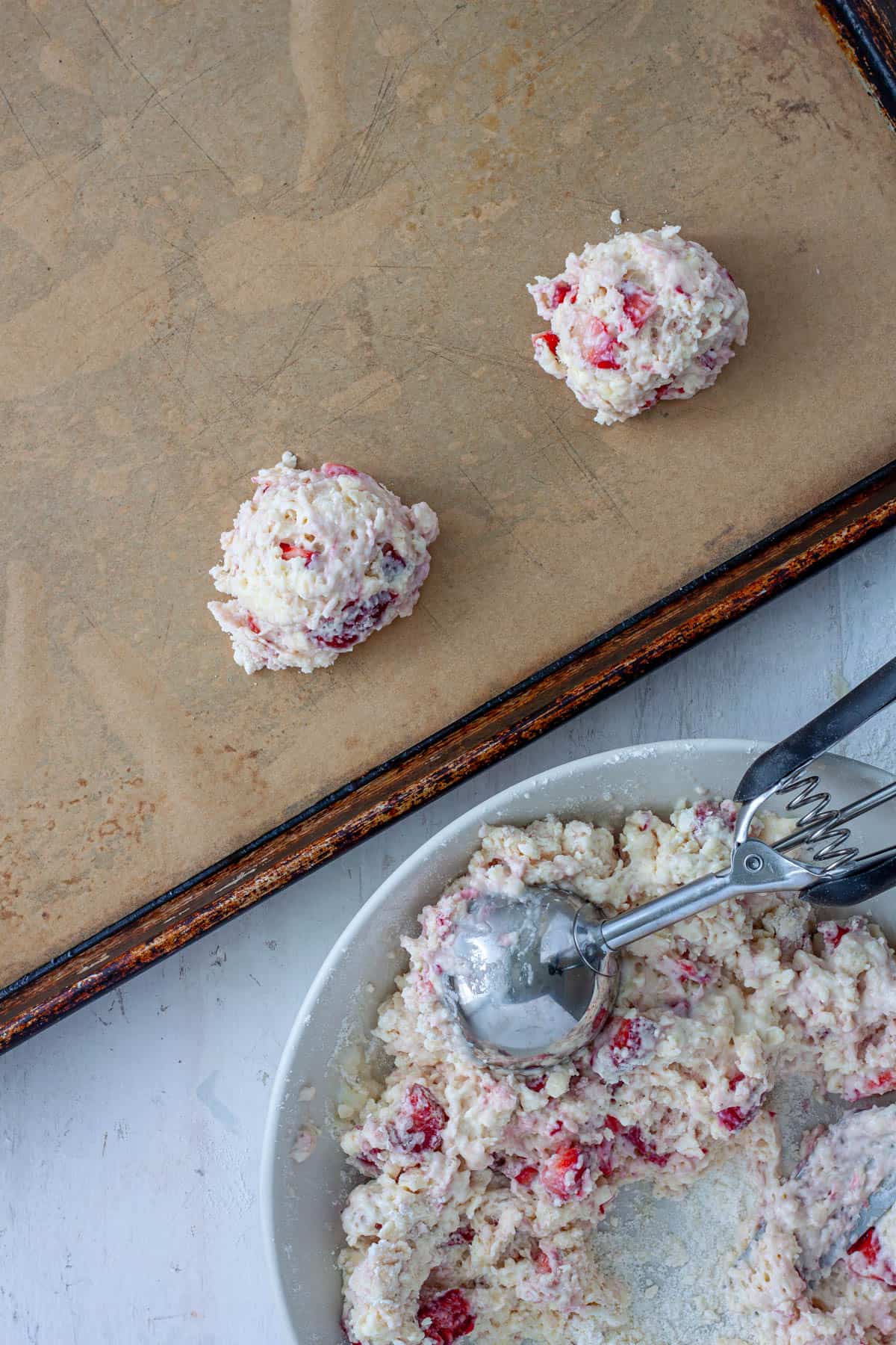 Strawberry biscuits getting scooped and placed on a parchment lined baking sheet.