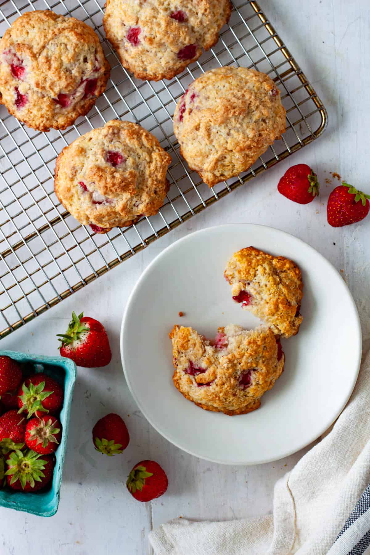 A strawberry biscuit broken in half on a small plate with more strawberry biscuits on a wire rack.