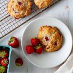 A strawberry biscuit on a small plate with more strawberry biscuits on a cooling rack.