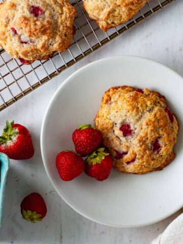 A strawberry biscuit on a small plate with more strawberry biscuits on a cooling rack.