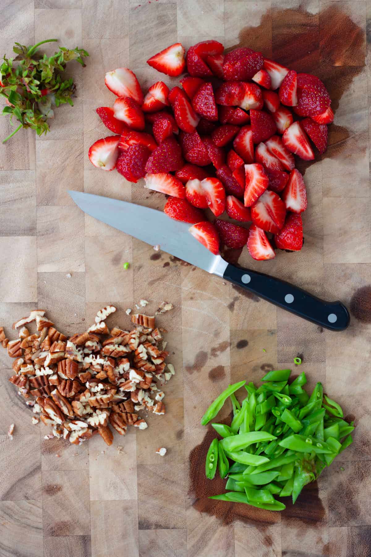 Strawberries, snap peas and pecans chopped on a wooden cutting board.