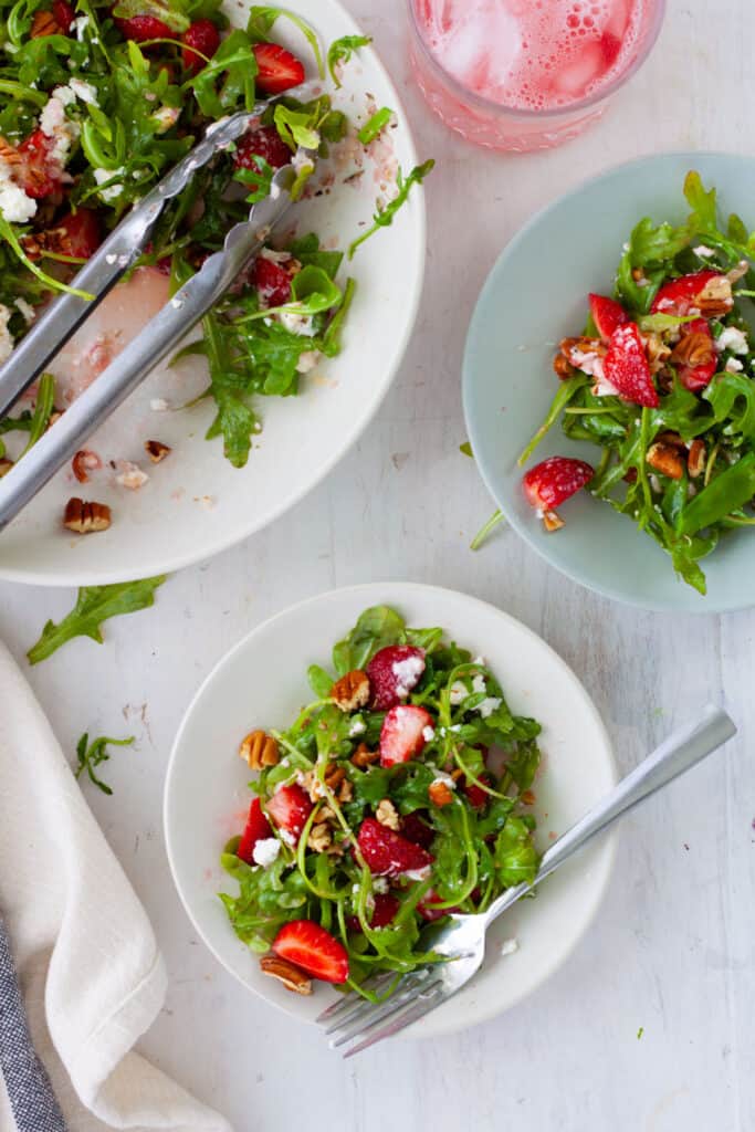 A bowl of strawberry and goat cheese salad with a couple servings on small plates.