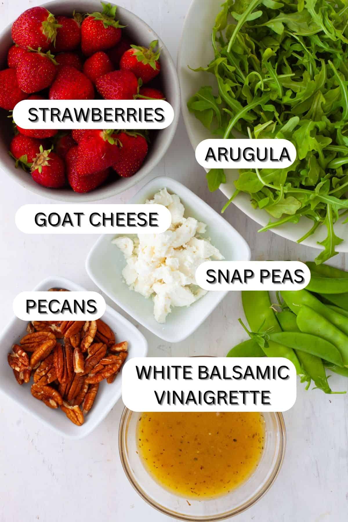 Ingredients for strawberry and goat cheese salad on a white table.