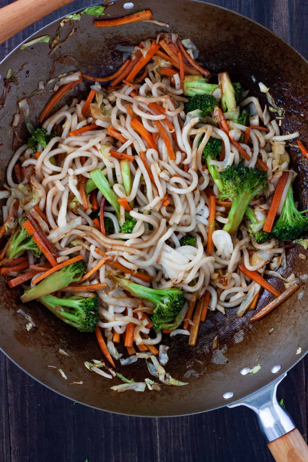 Udon noodles and vegetables cooking in a wok.