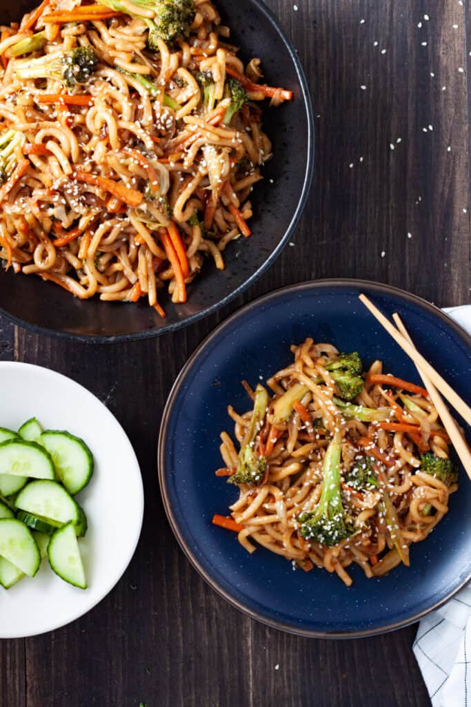 A serving bowl and a small plate with teriyaki udon with vegetables.