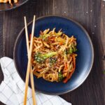 A plate with teriyaki udon and vegetables with chopsticks on the side of the plate.